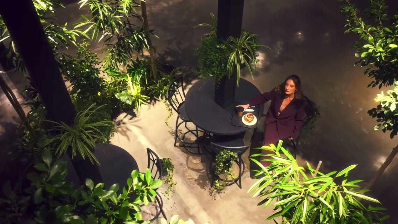 A guest at a round table with coffee and a pastry, seen from above among the palms